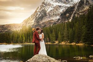 Couple de mariés devant un lac avec une forêt et une montagne en fond