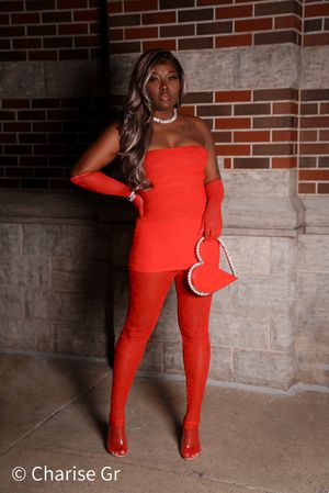Fashion model wearing all-red ensemble with heart purse poses against industrial brick backdrop.