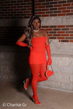 A fashionable red ensemble with matching accessories photographed against an urban brick wall background.