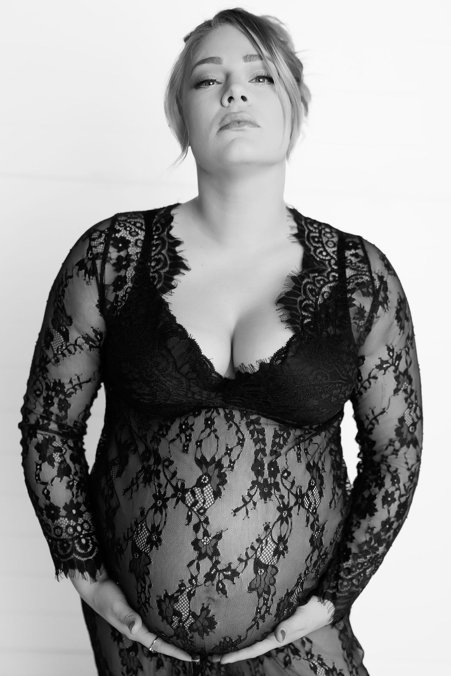 Black and white maternity photo showing a figure in lace lingerie posing against a plain backdrop.