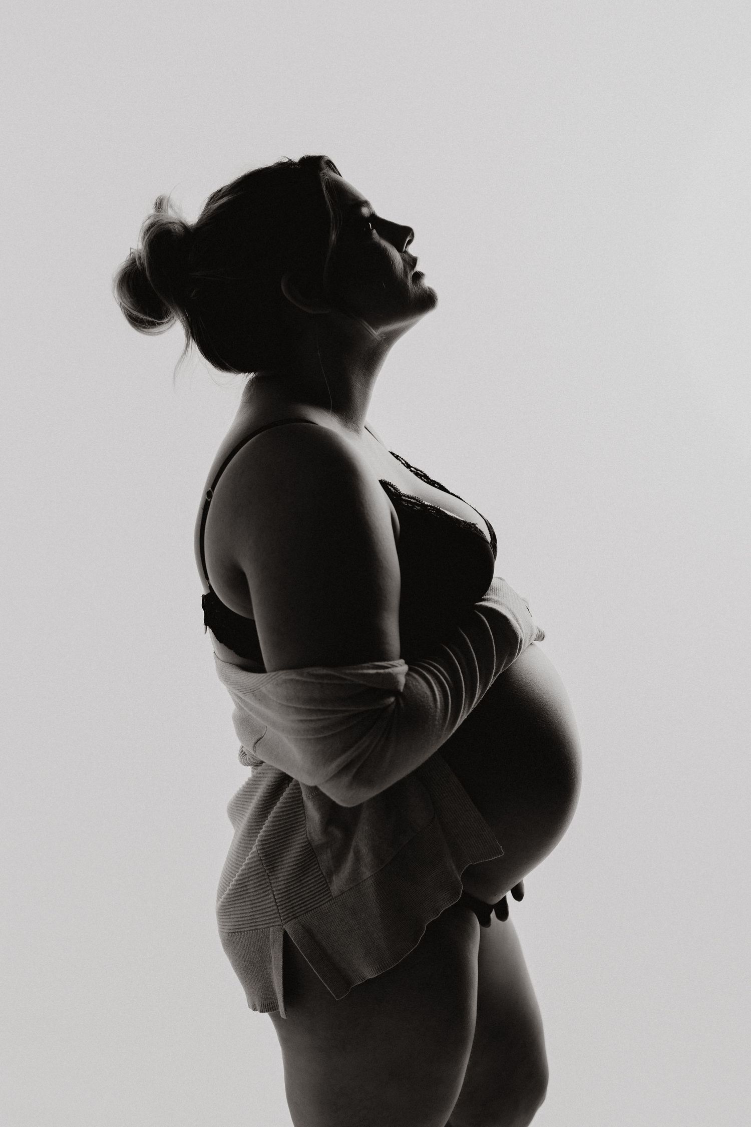 Artistic black and white silhouette maternity photo showing a pregnant figure in profile with a flowy wrap.