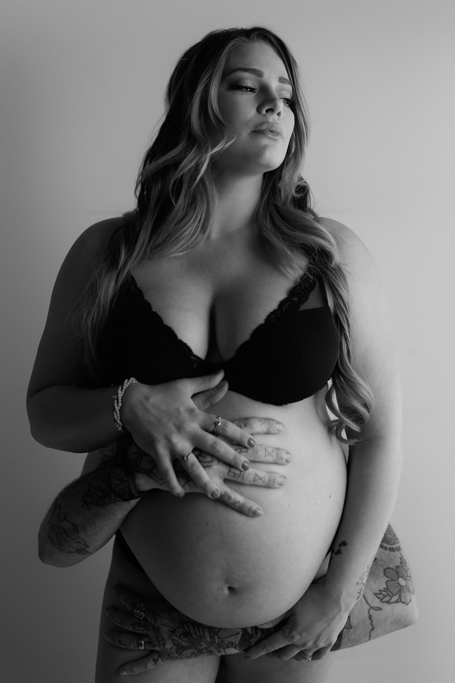 A black and white artistic maternity photo showing a woman in intimate apparel embracing her pregnant belly.