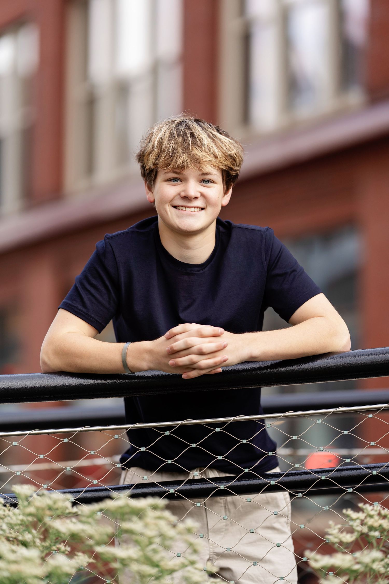 Senior photo of a boy leaning on a fence with a city building behind him taken by Milwaukee senior photographer Rachel Dickman.