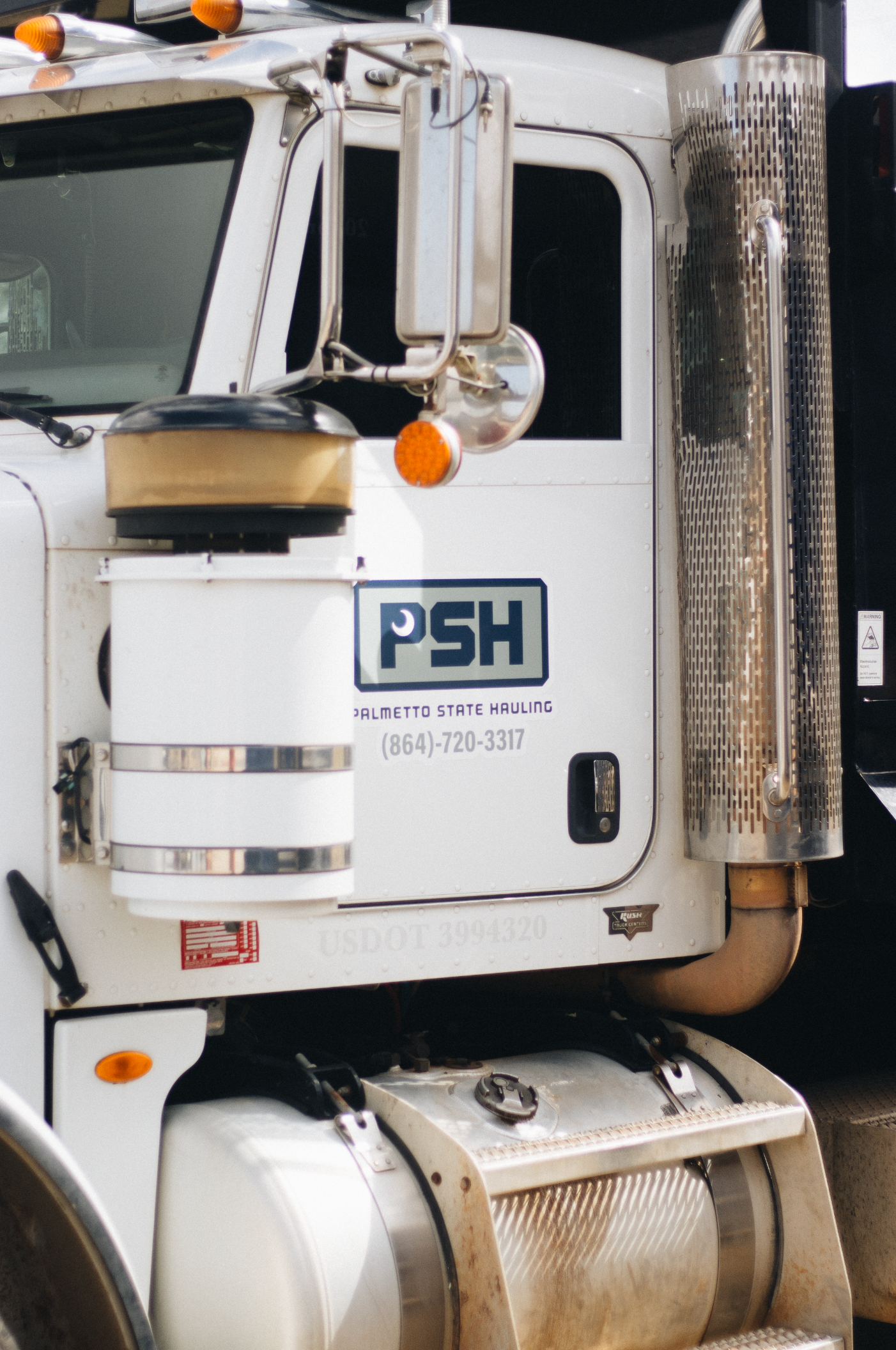 Close-up view of a white PSH branded truck cab with chrome exhaust stack.