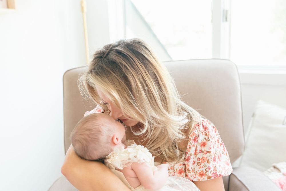 A close up of a mother kissing her newborn baby in a colorful nursery.