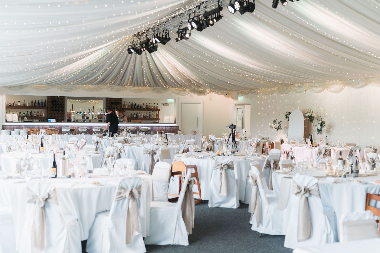 An elegant white wedding reception venue with draped ceiling, covered chairs and soft blue accents throughout the space.