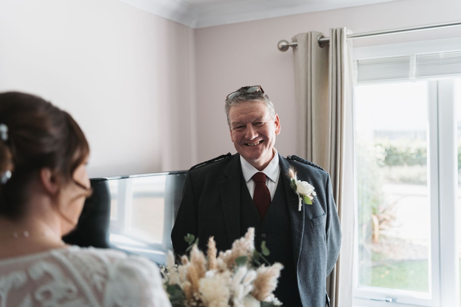 An emotional moment between two people during a wedding celebration with a white floral bouquet and natural window lighting.