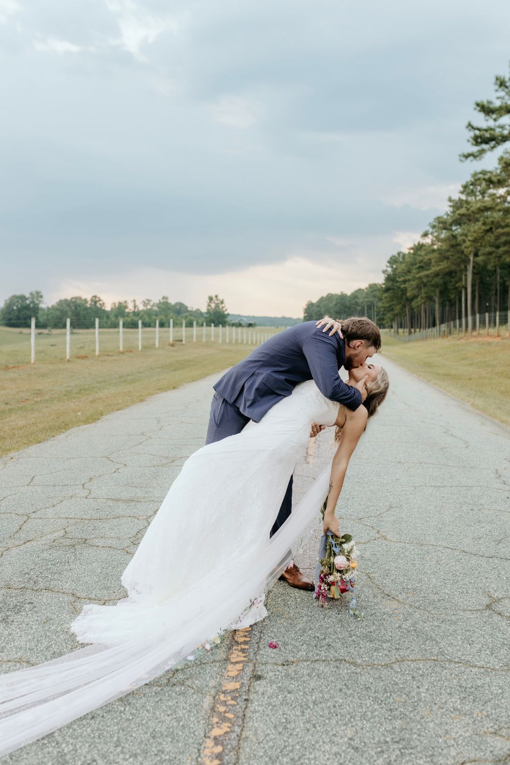 A romantic wedding couple sharing a kiss on a stone pathway surrounded by a meadow and pine trees.