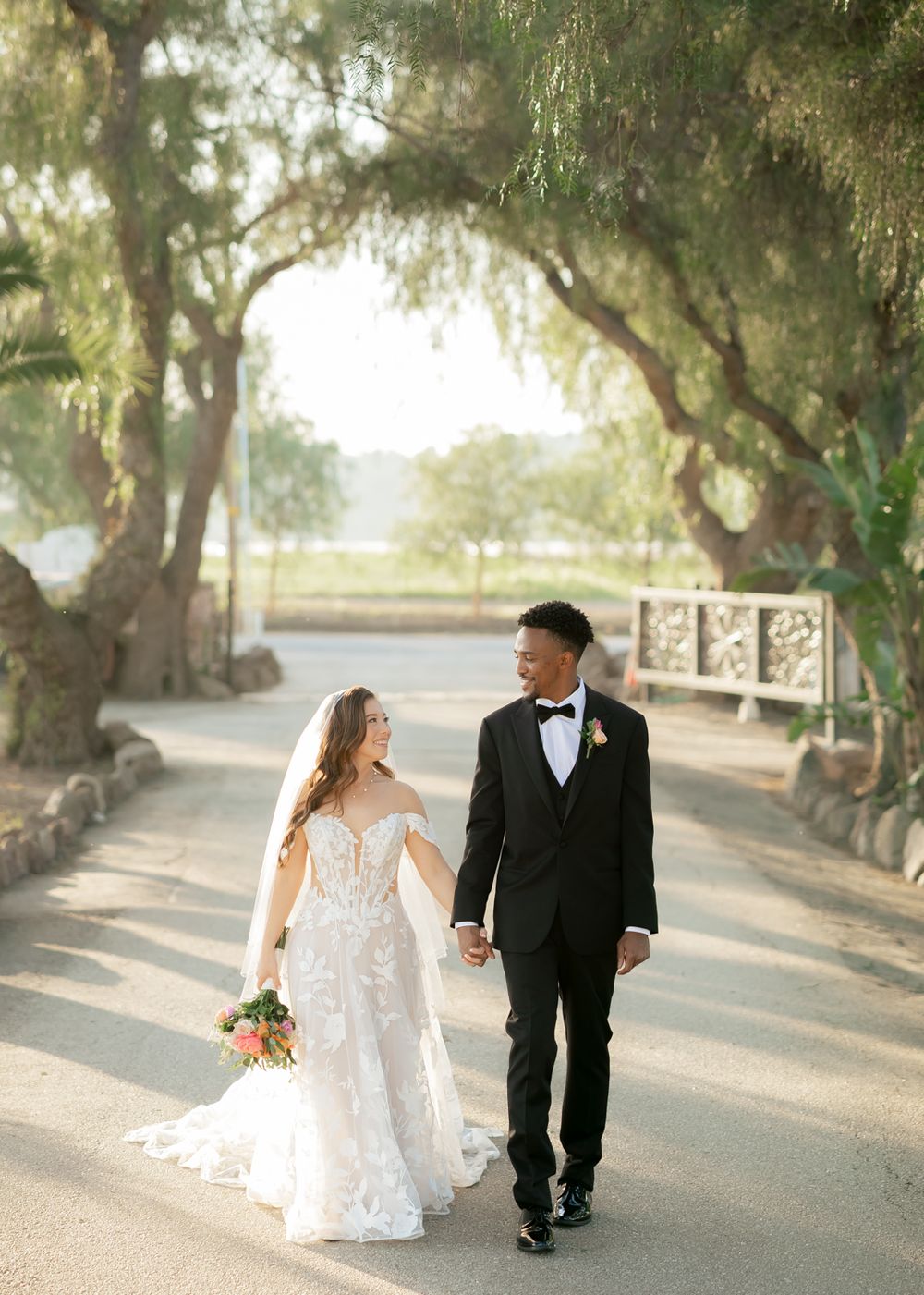 A romantic wedding portrait on a tree-lined path in golden afternoon light.