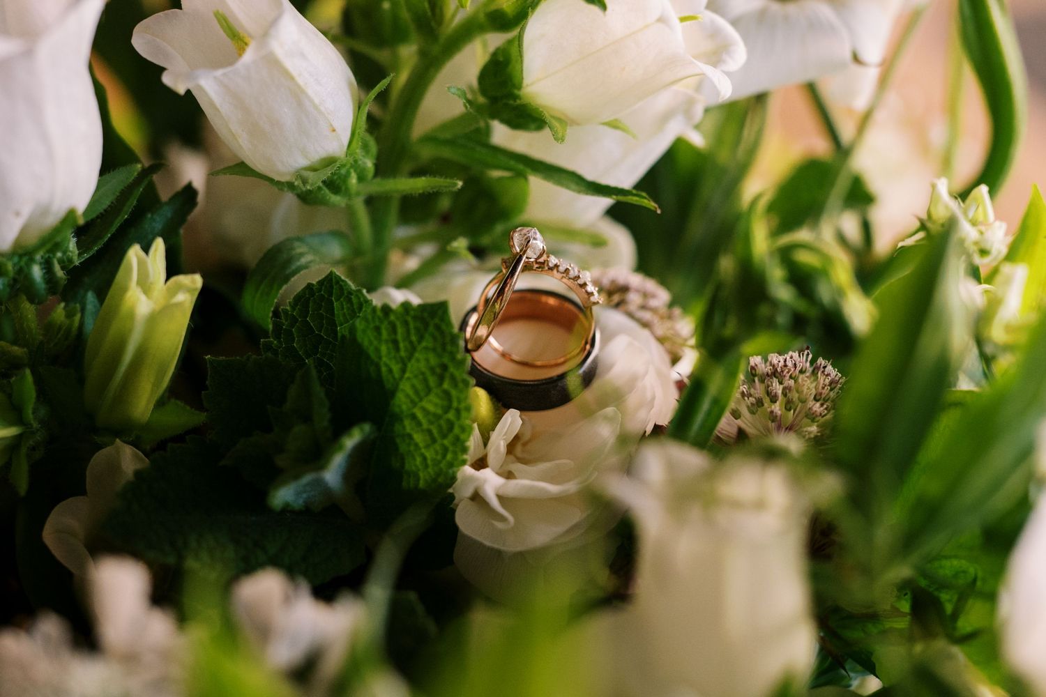 Wedding rings nestled among white tulips and greenery in an elegant floral arrangement.