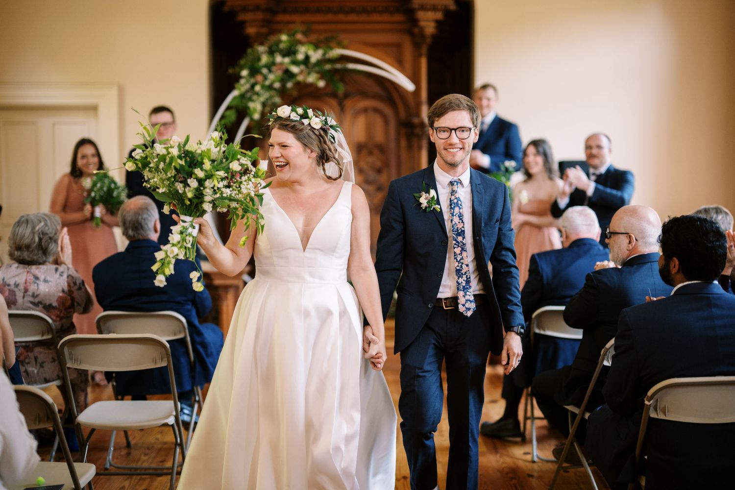 Joyful wedding moment captured during indoor ceremony with decorative arch and seated guests.