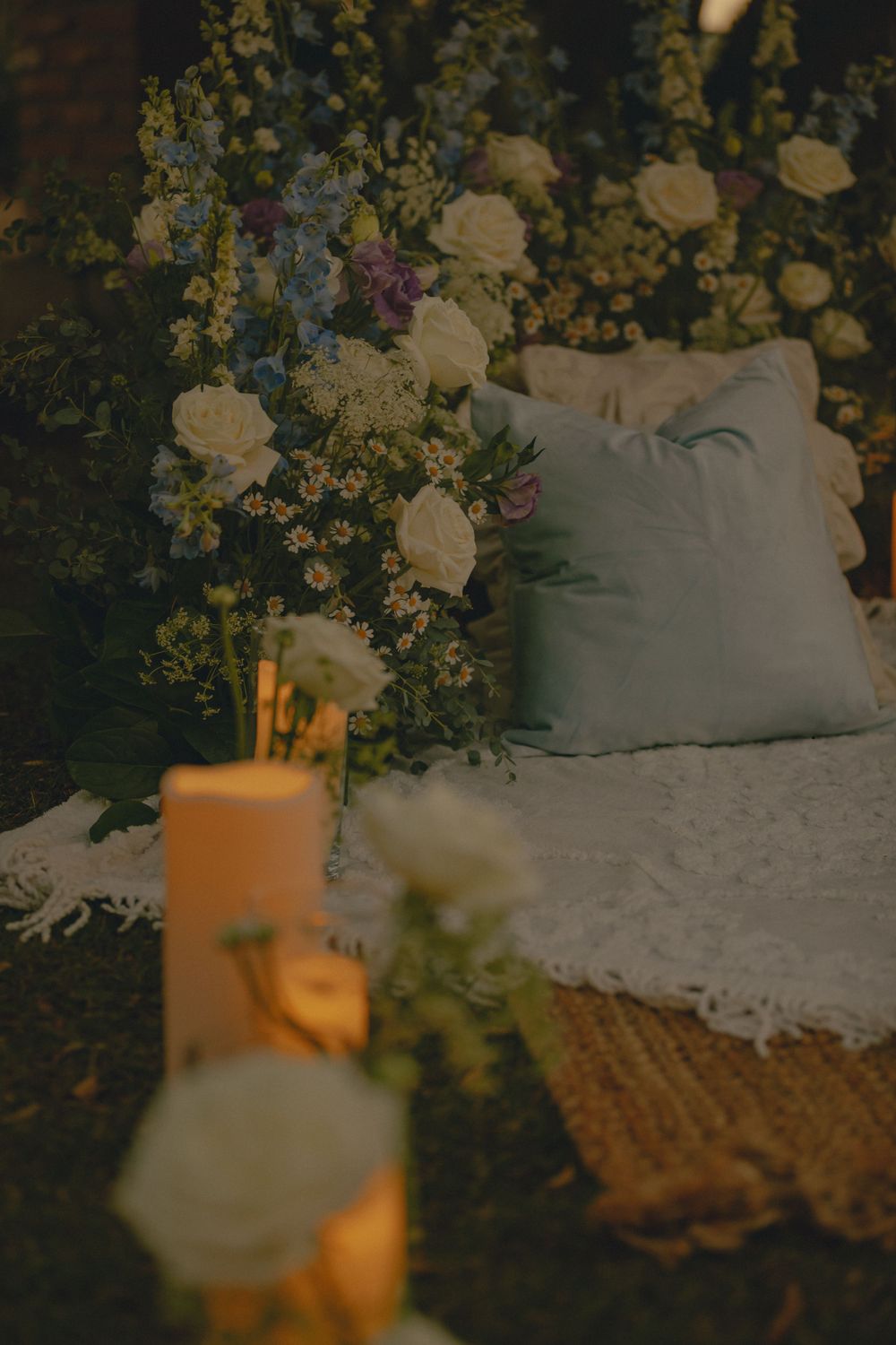 Cozy cushioned picnic decorated with romantic floral arrangements and glowing candles against a dark background.