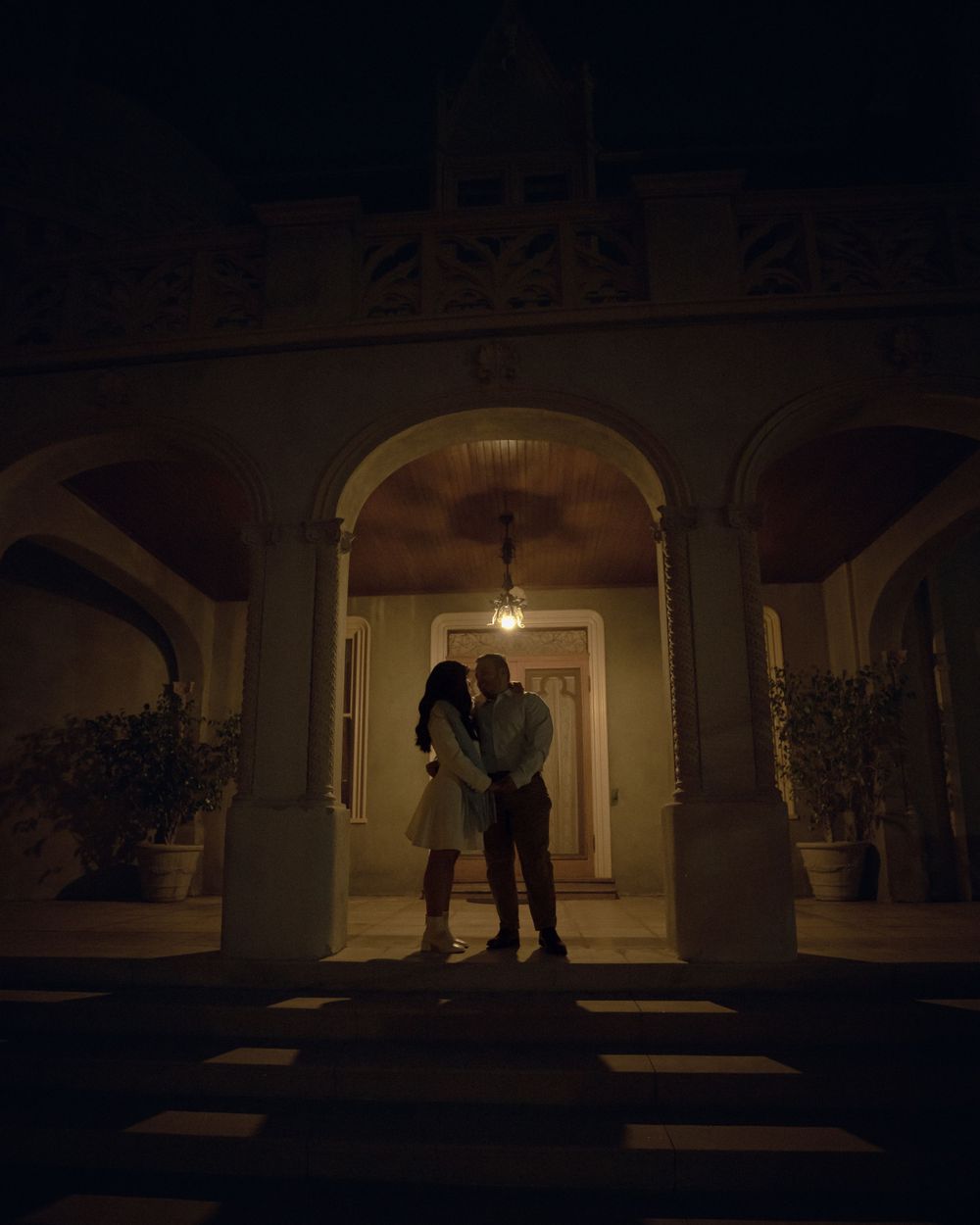 A silhouetted couple stands in an illuminated archway at night with architectural columns framing the romantic scene.