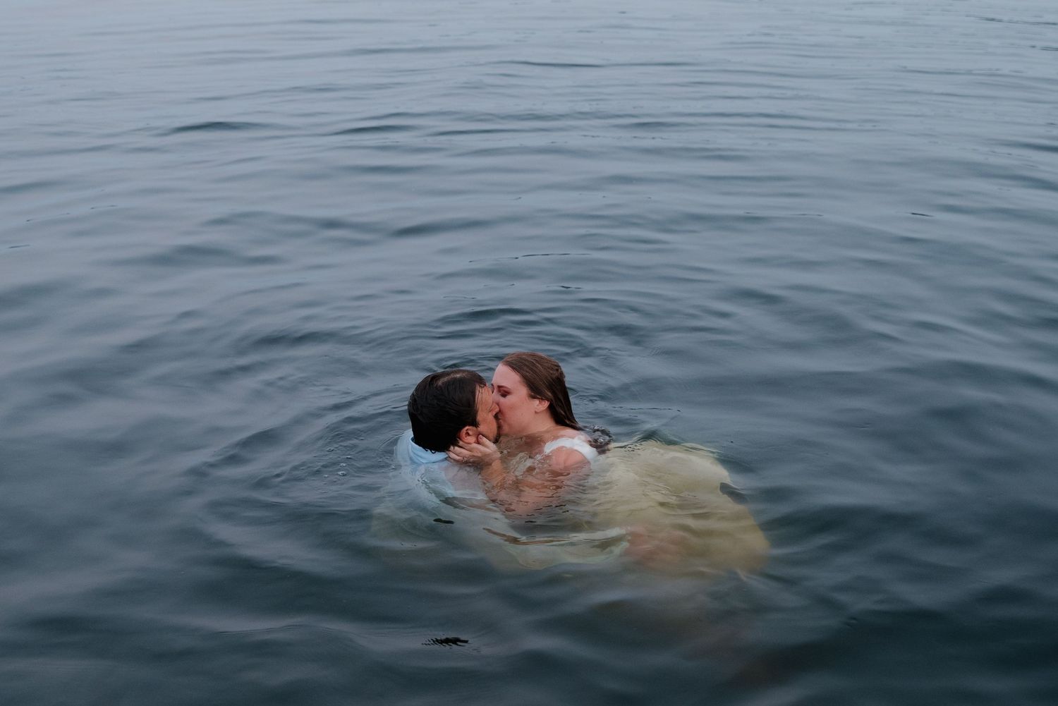 A couple embraces while floating in calm, misty waters during an intimate moment.