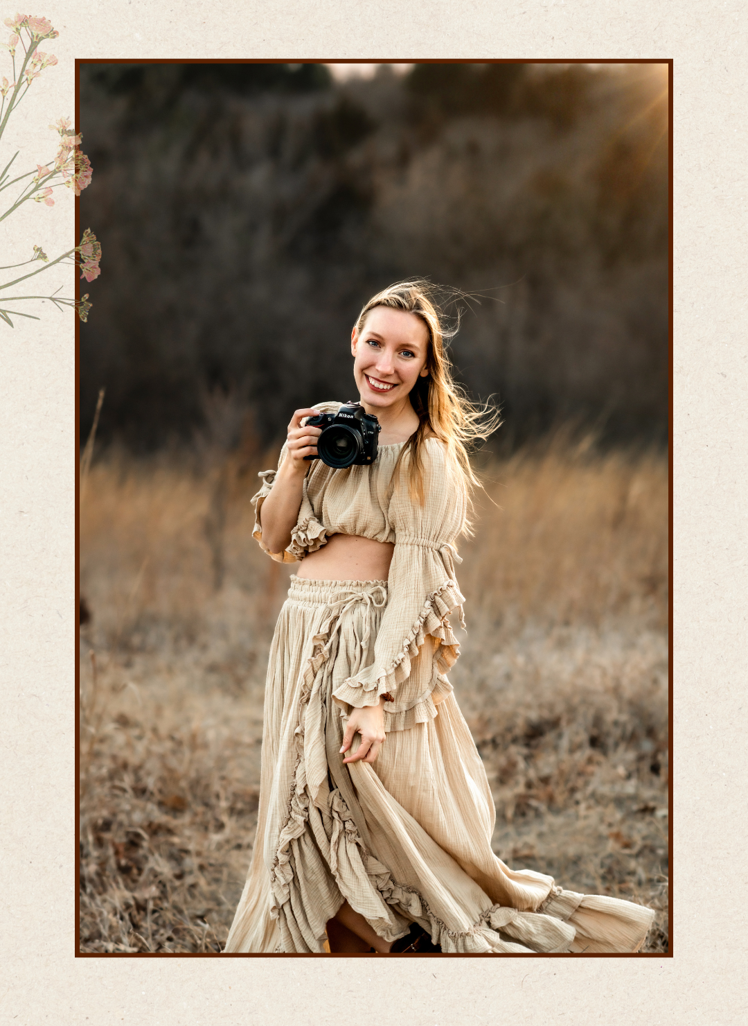 Photographer wearing flowing beige dress holds vintage camera in autumn field with warm moody lighting.