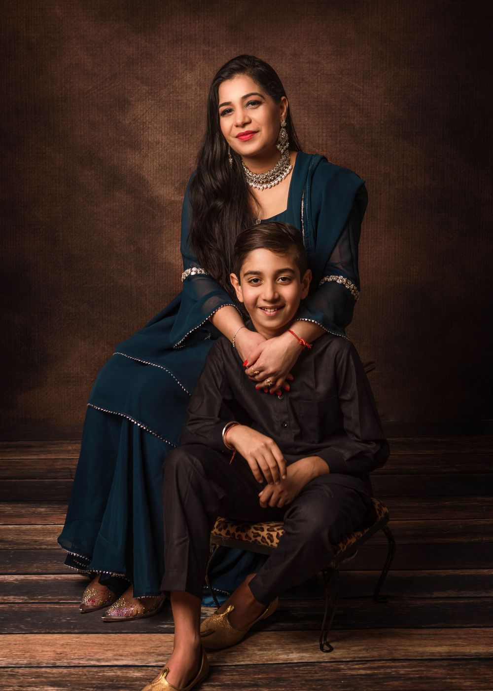 Portrait of a family in traditional Indian attire posing together on wooden floor against dark brown backdrop.