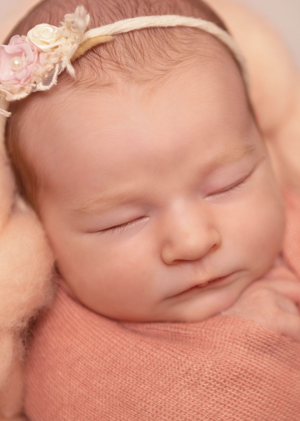 Peaceful sleeping baby wearing a delicate floral headband rests on soft peach-colored fabric.