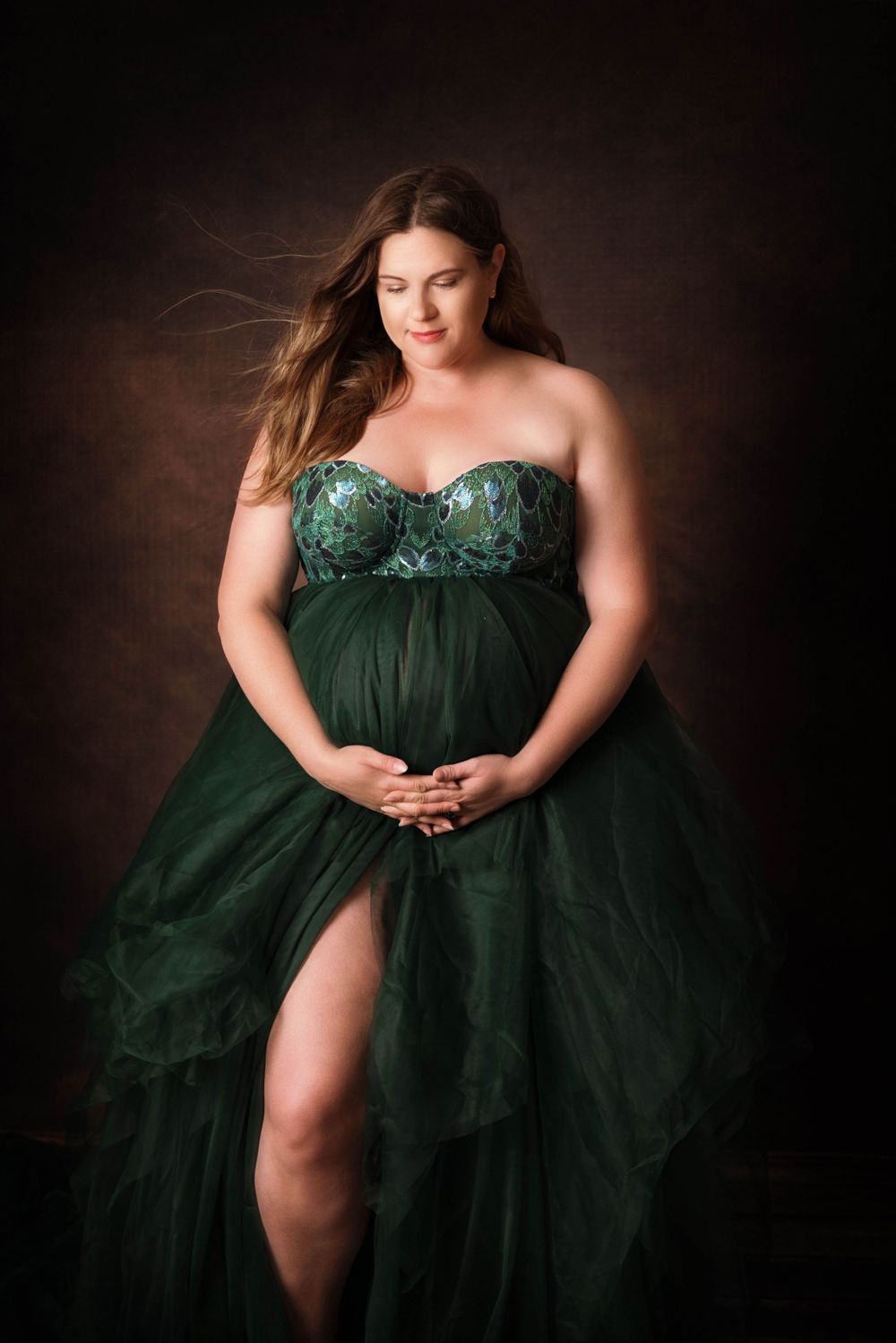 A flowing emerald green tulle gown with sweetheart neckline and high slit against a dark moody background.