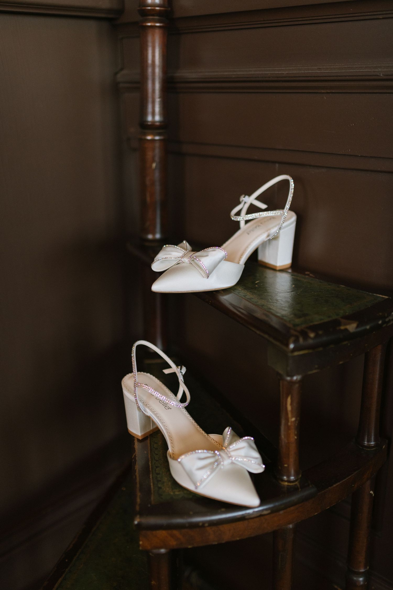White bridal heels with bow details displayed on vintage wooden stairs.