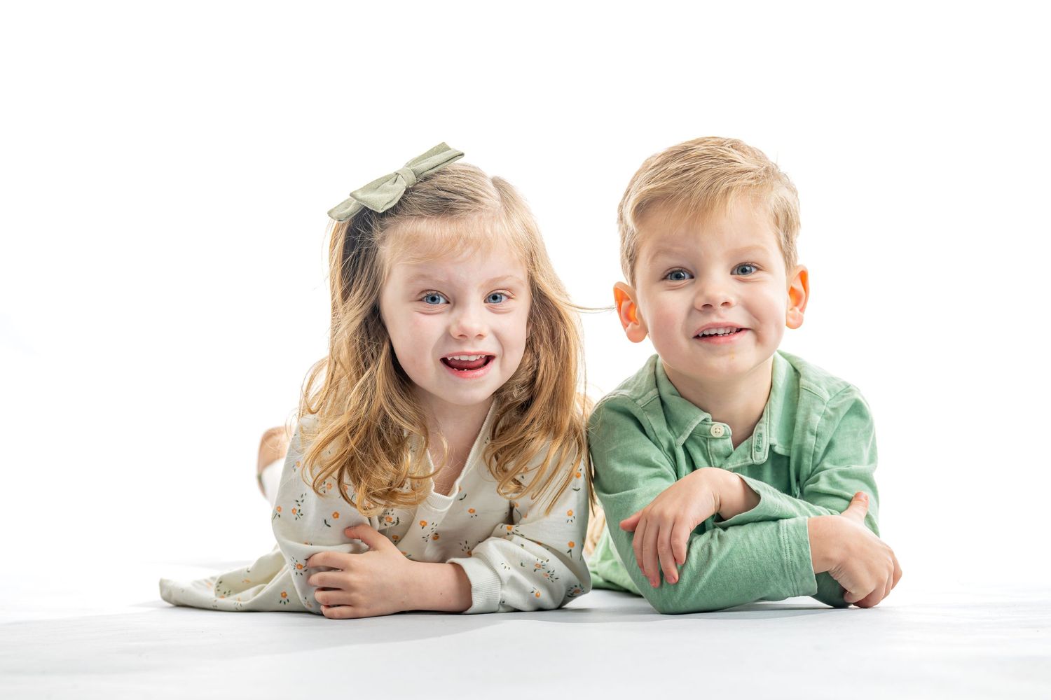 Two children lying on their stomachs wearing casual clothes on a white background.