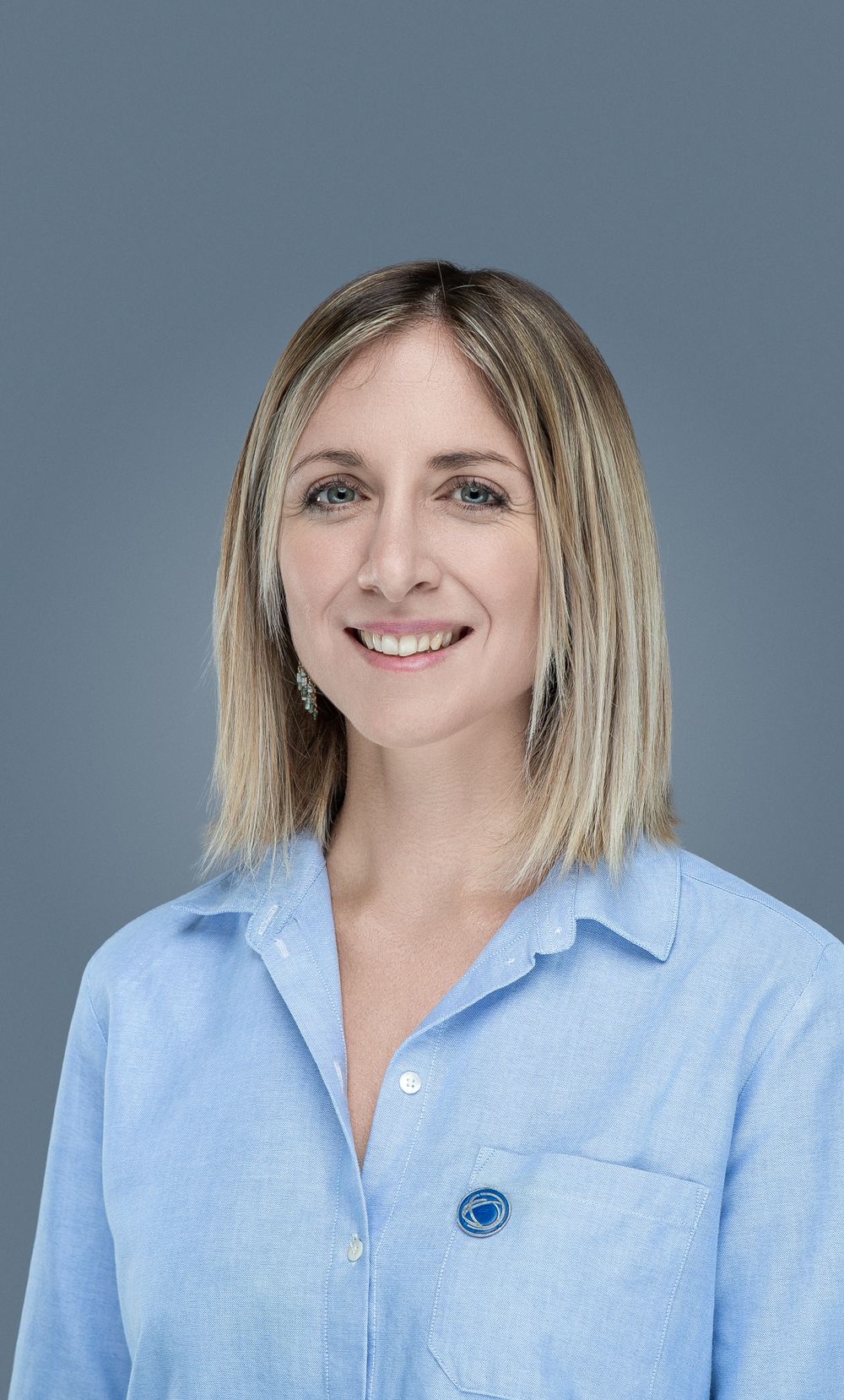 Professional headshot of someone wearing a light blue button-down shirt against a grey background.
