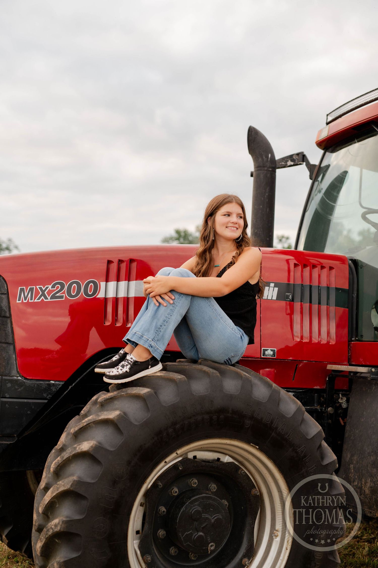 Someone in casual attire sits comfortably on the massive tire of a red MX200 tractor.