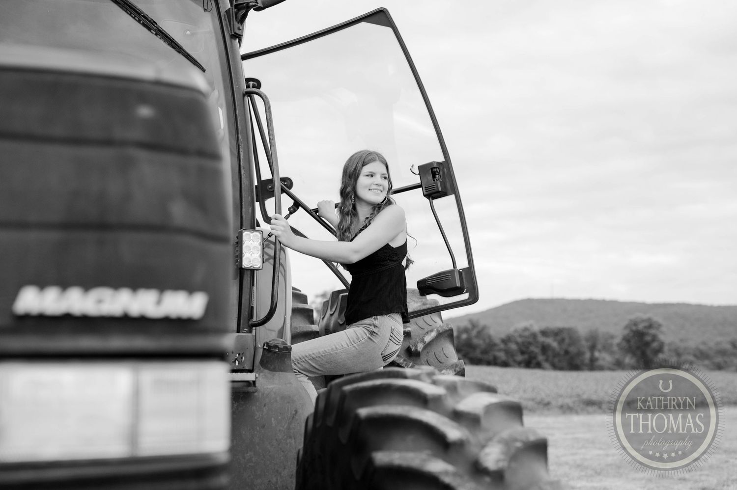 Black and white photo of someone sitting on the wheel of a Magnum tractor at dusk.