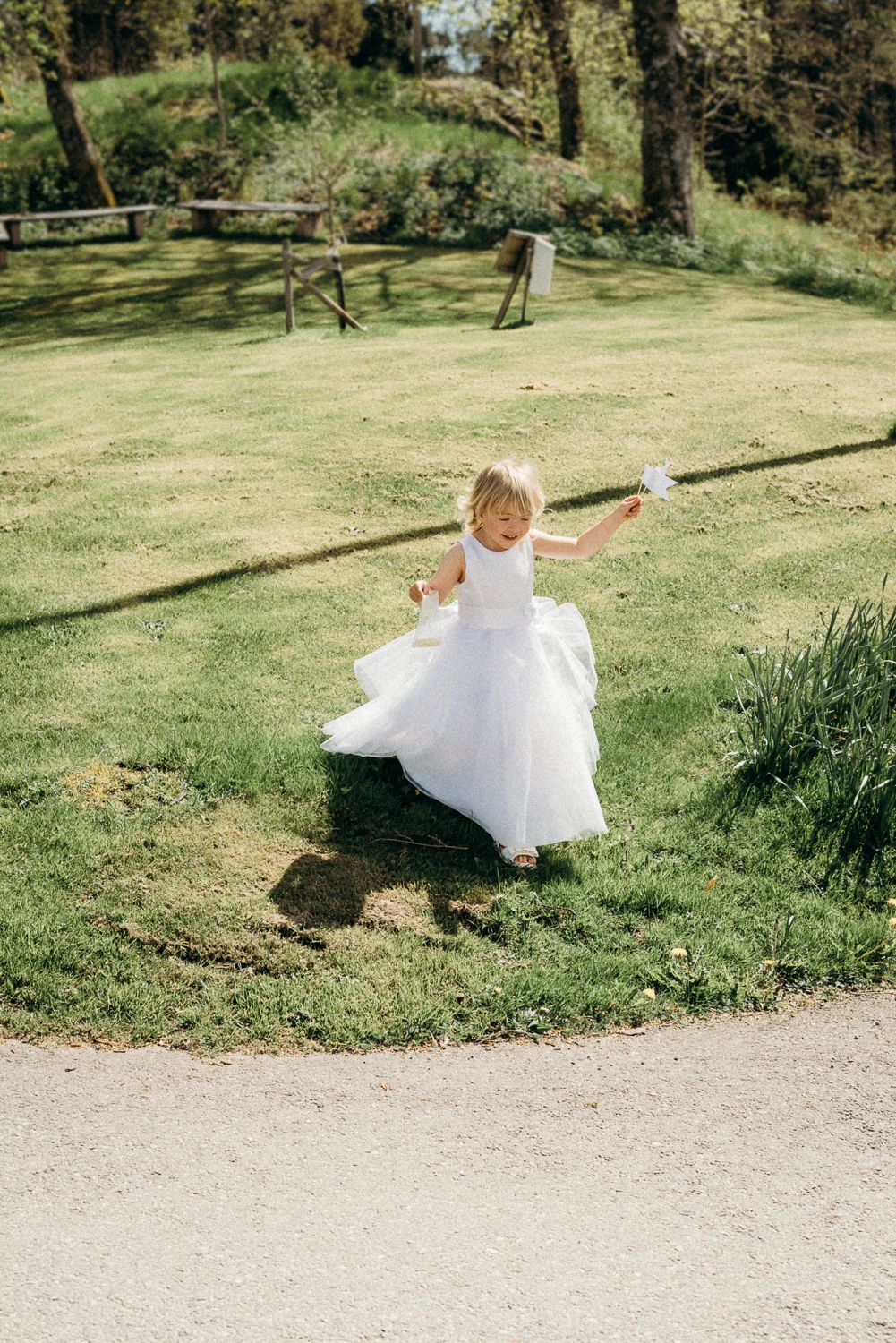Small figure in flowing white dress twirls joyfully on a sunny grassy lawn near a winding garden path.