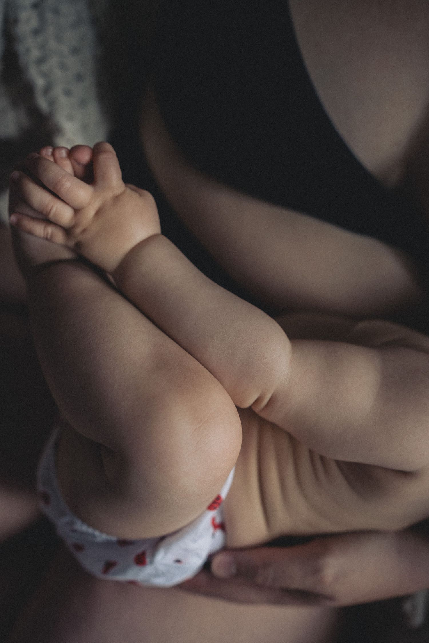 Close up detail of baby legs and feet being gently held against a dark background.