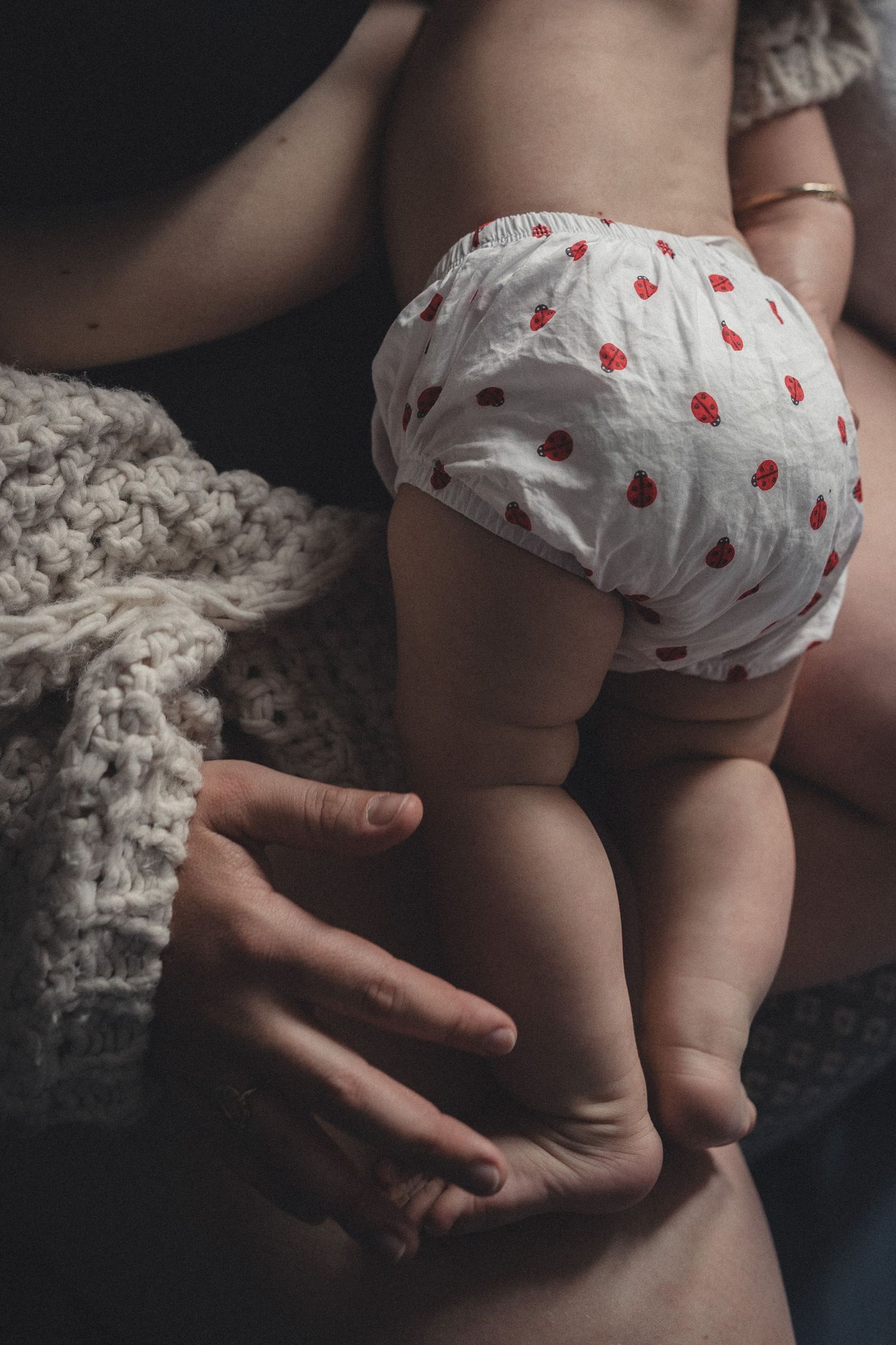 Close-up of baby wearing polka dot diaper with caregiver's hands providing gentle support.