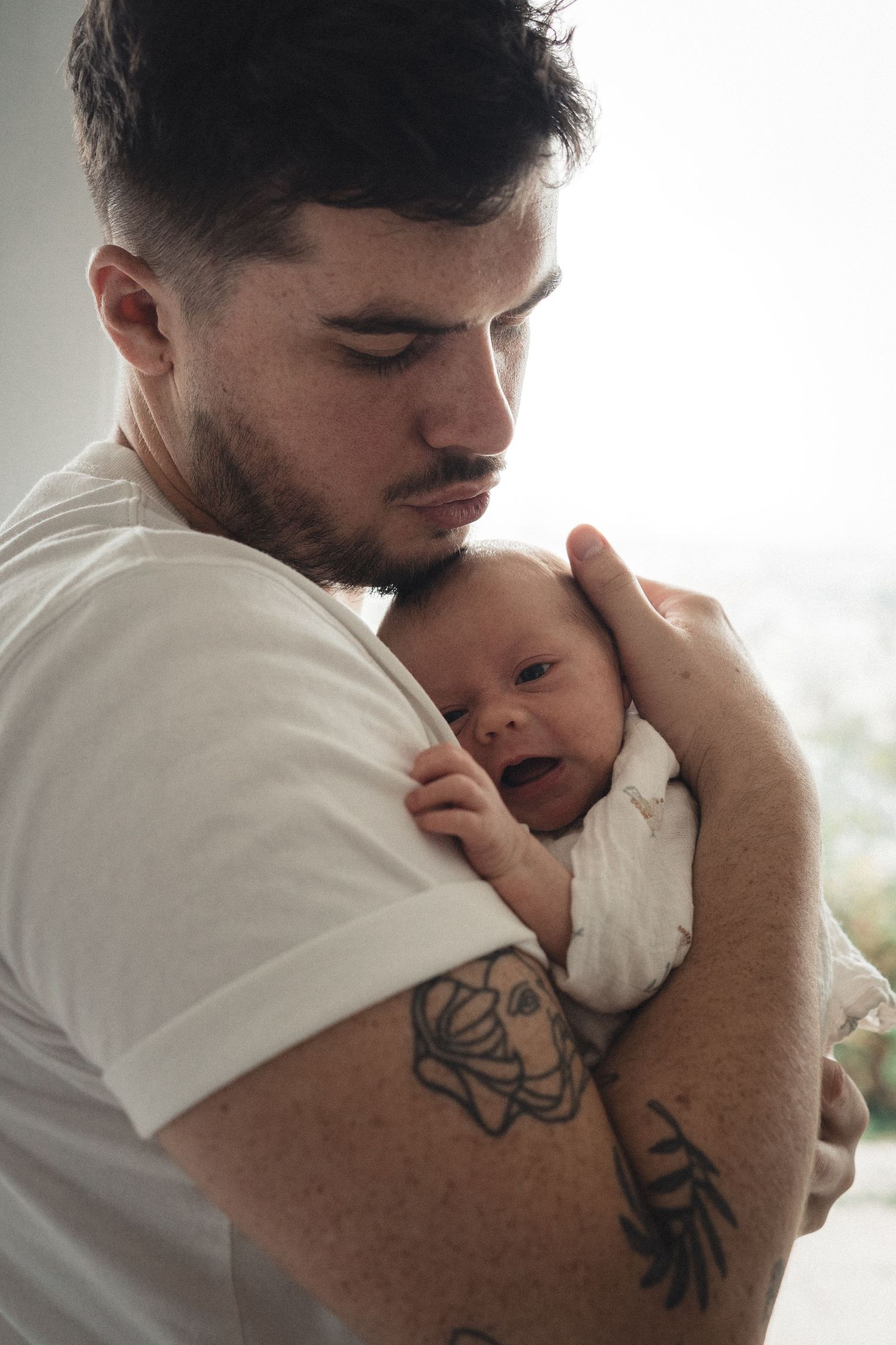 Un moment tendre entre un parent et un nouveau-né, montrant une étreinte douce et des tatouages sur les bras.
