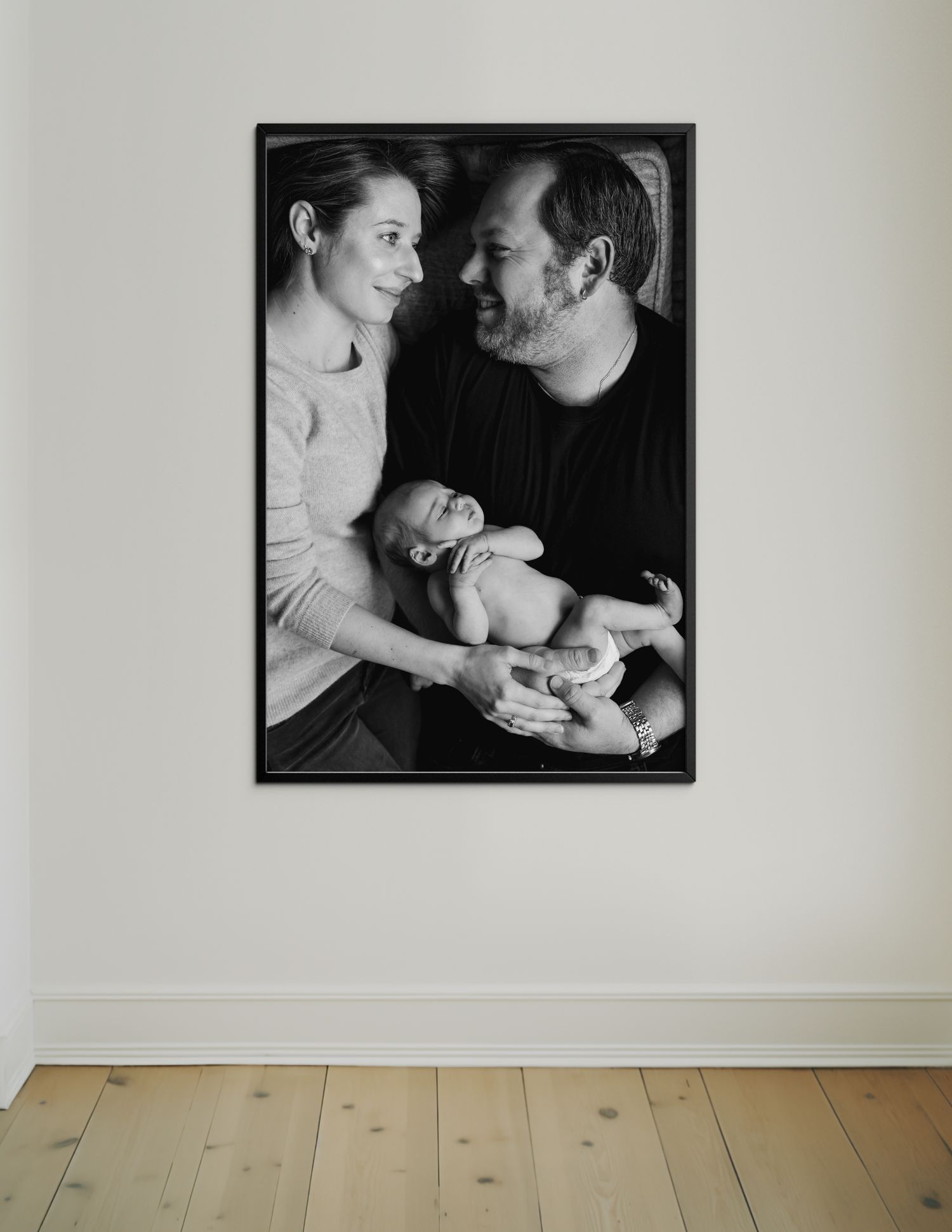 A large black and white family photo portrait hung on a white wall above light wooden flooring.