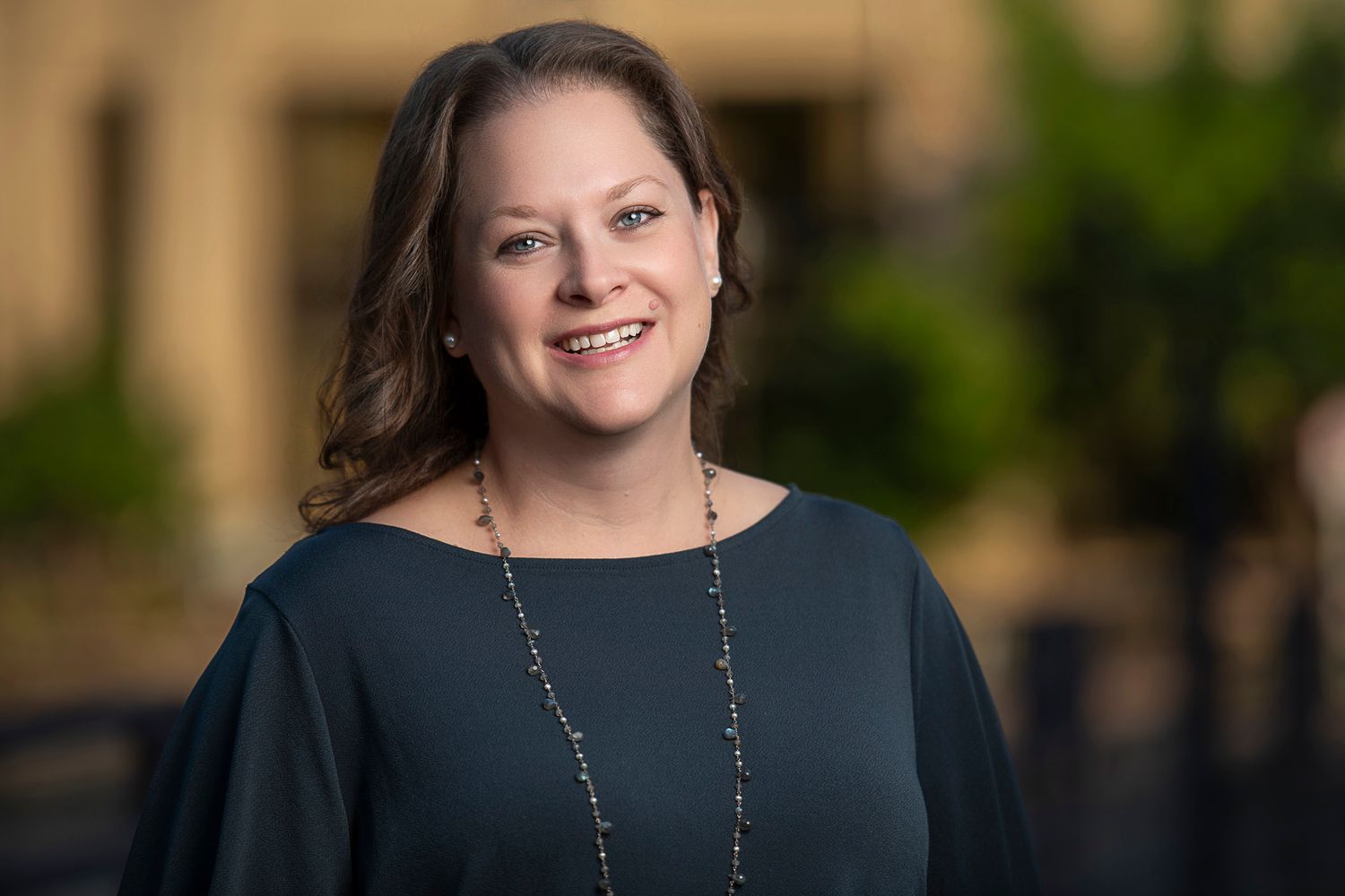 Professional headshot of someone in a navy top against a blurred background.
