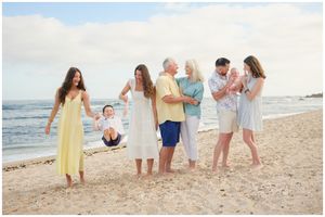 A group enjoying a casual gathering on the beach at sunset wearing light colored clothing while standing near the ocean.