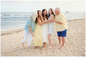 A group wearing light summer clothing laughs together while standing on a sandy beach at sunset.
