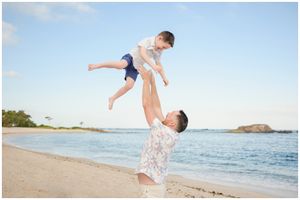 Two people share a joyful moment on the beach as one lifts the other high into the air against the ocean backdrop.