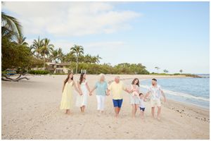 Group holds hands while walking along a tropical beach with palm trees and ocean views in Hawaii.