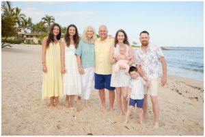 Family group poses together on a tropical beach at sunset with palm trees and ocean in the background.