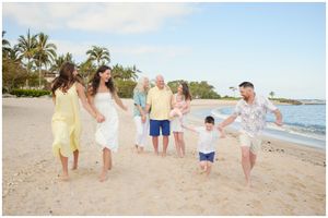 Multi-generational family enjoying a playful moment together while walking on a tropical beach at sunset.