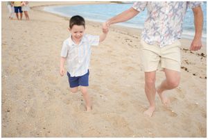 A child and adult walking together on a sandy beach holding hands.