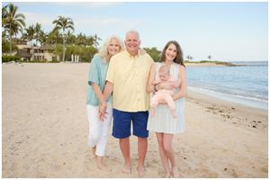 A group stands together smiling on a tropical beach with palm trees and ocean in the background.