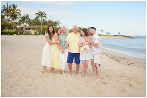 A family enjoys a sunset photoshoot on a tropical beach with palm trees and ocean views.