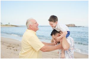 Joyful family shares playful moment together on a sunny beach with ocean waves in the background.