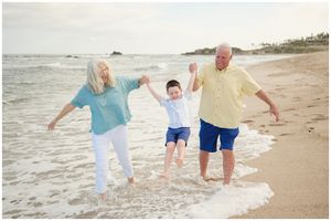 Three people playing and jumping together on a sandy beach by the ocean waves at sunset.