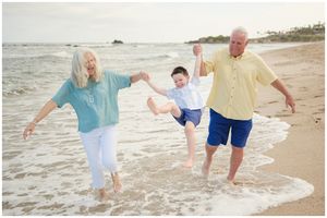 Family plays in the shallow ocean waves on a sunny beach while holding hands and splashing together.