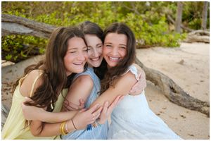 Three friends embrace while smiling and laughing together at the beach surrounded by nature.