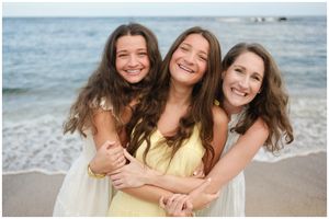 Three friends sharing joyful laughter together on a sunny beach with ocean waves in the background.