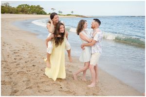 Two couples enjoy a playful moment together on a sunny beach with waves lapping at the shoreline.