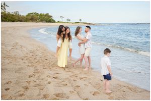 A group walks together along a sandy beach shoreline with calm ocean waters and tropical trees in the background.