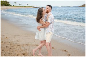 A couple shares a romantic moment on a sandy tropical beach with blue ocean waves in Hawaii.
